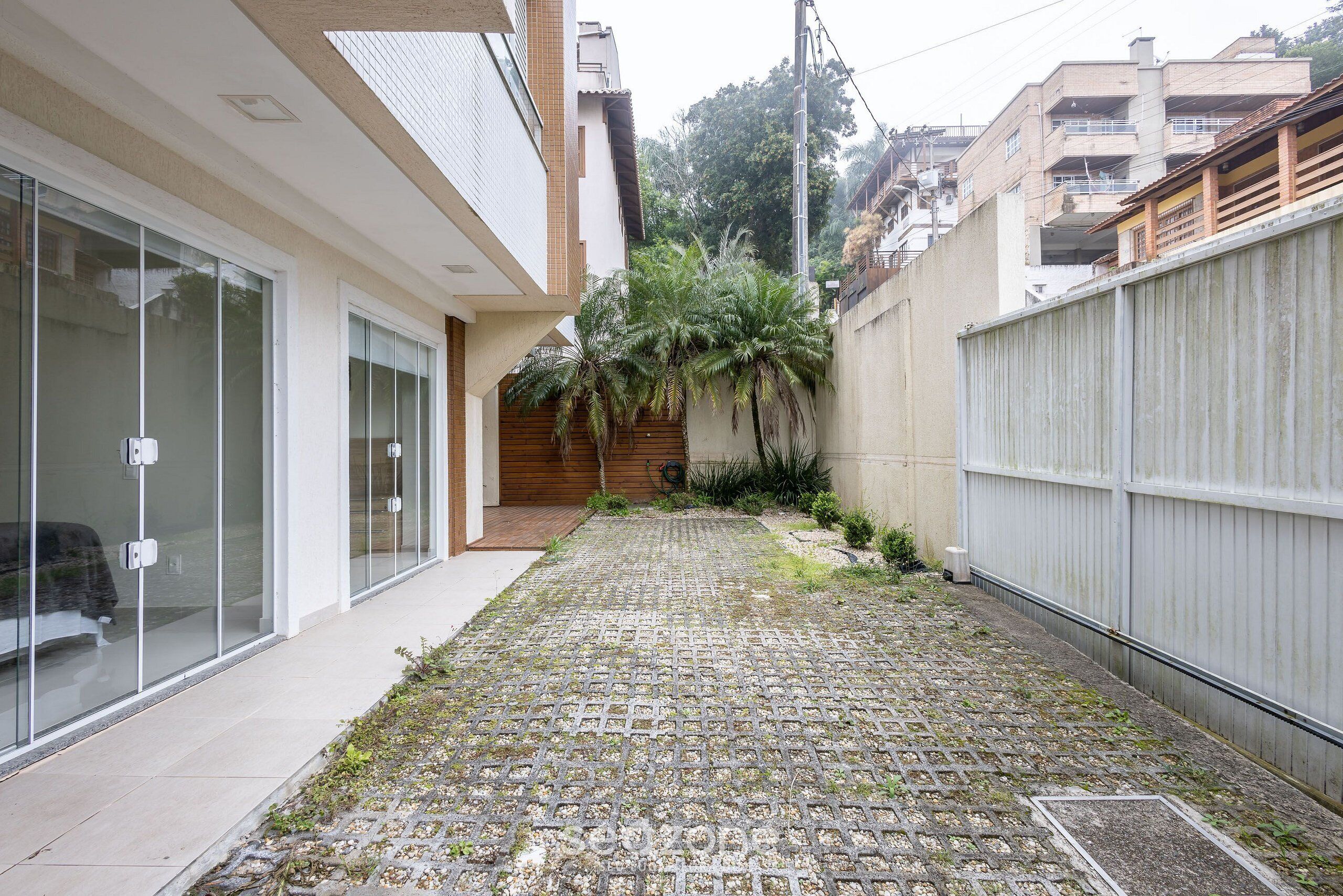Une cour étroite avec un chemin pavé de pierres, une clôture en bois et un bâtiment doté de grandes portes vitrées.