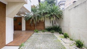 A modern courtyard with a wooden deck, a palm tree, and a concrete wall. - 3BR Apt w/ BBQ 290m From Beach Pic0125 (Bombinhas)
