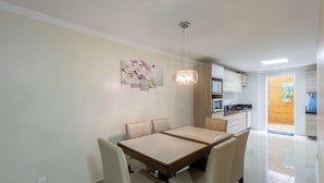 A dining area with a table and chairs, a hanging light fixture, and a kitchen in the background. - 3BR Apt w/ BBQ 290m From Beach Pic0125 (Bombinhas)