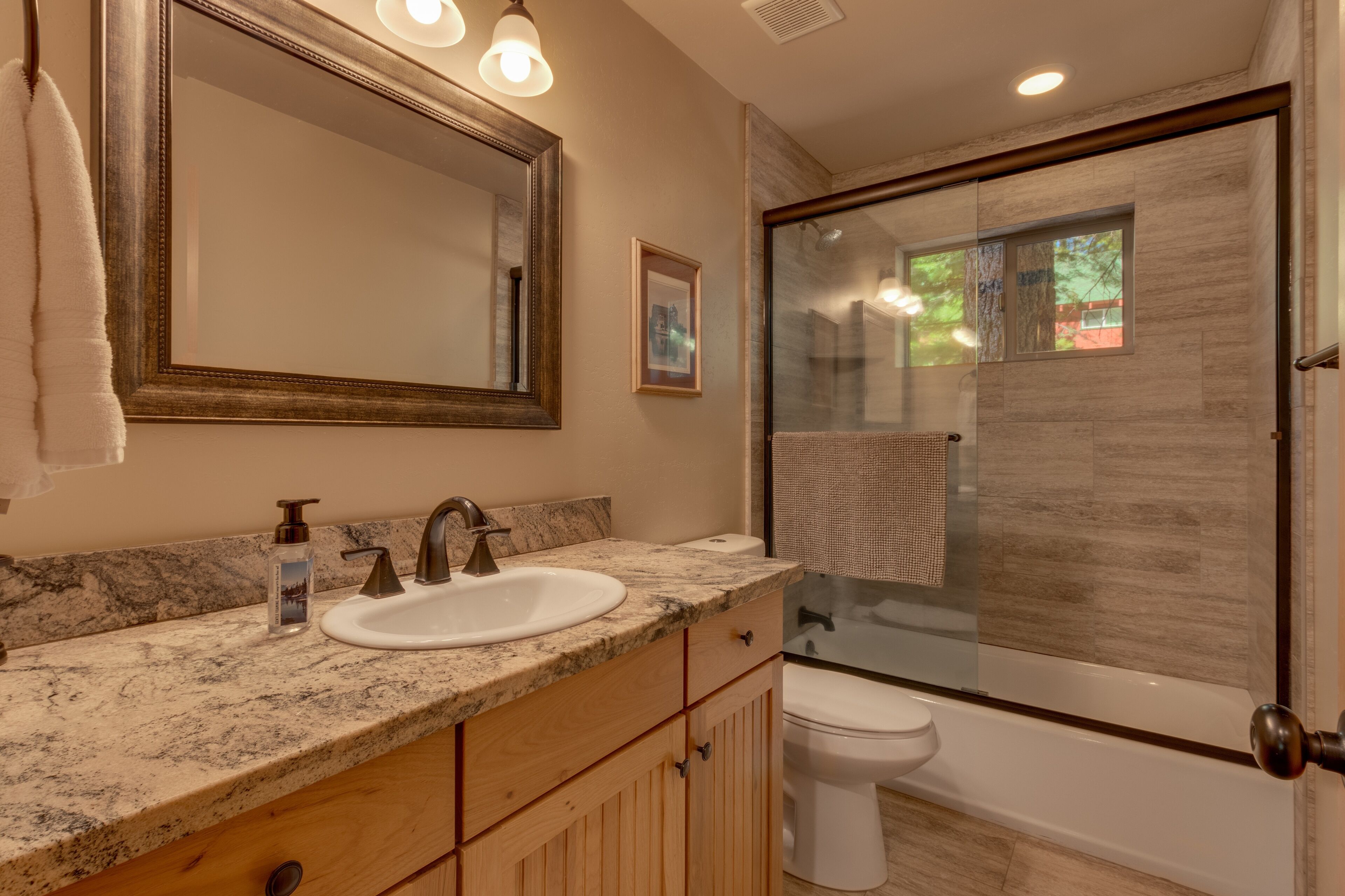 A bathroom with a marble countertop, a sink, a mirror, a toilet, and a glass-enclosed shower area.