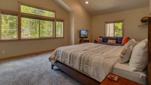 A bedroom with a large bed, a TV, and a seating area with a view of trees. - The Westlands Lodge 1135ac 4 Bedroom Home (South Lake Tahoe)