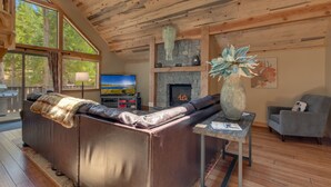A cozy living room with a stone fireplace, leather sofa, and a television. - The Westlands Lodge 1135ac 4 Bedroom Home (South Lake Tahoe)