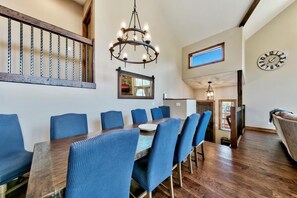 A dining area with a wooden table, blue upholstered chairs, a chandelier, and a clock on the wall. - 1008c Mountain View Retreat 5 Bedroom Home (South Lake Tahoe)