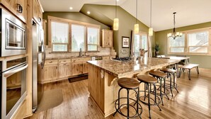 A modern kitchen with wooden cabinets, stainless steel appliances, a large island with bar stools, and large windows allowing natural light. - 1376md Angora View 4 Bedroom Home (South Lake Tahoe)