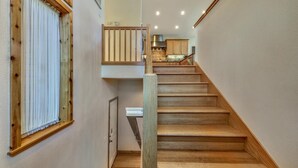 A wooden staircase leading to a kitchen area with wooden cabinets and a window with a curtain.