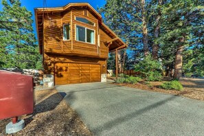 A wooden cabin with a garage, surrounded by trees.