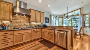 A spacious kitchen with wooden cabinets, a stainless steel range hood, and a large island with a dishwasher.
