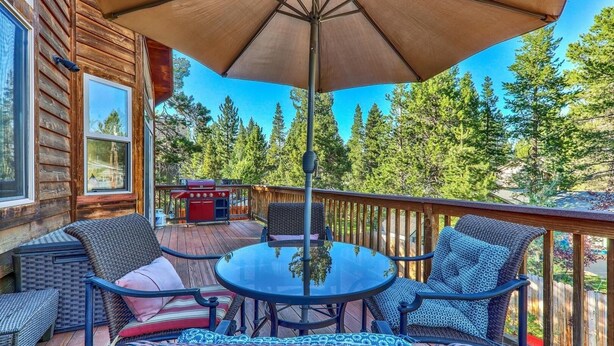 A wooden deck with a round table and chairs, a barbecue grill, and a large umbrella.