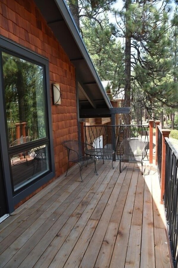A wooden deck with outdoor furniture, a large window, and a view of trees.