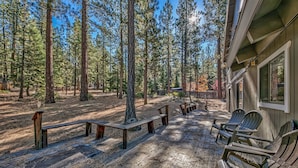A wooden deck with benches and chairs, surrounded by tall pine trees. - 121m The Meadow Drive Home 5 Bedroom Home (Stateline)