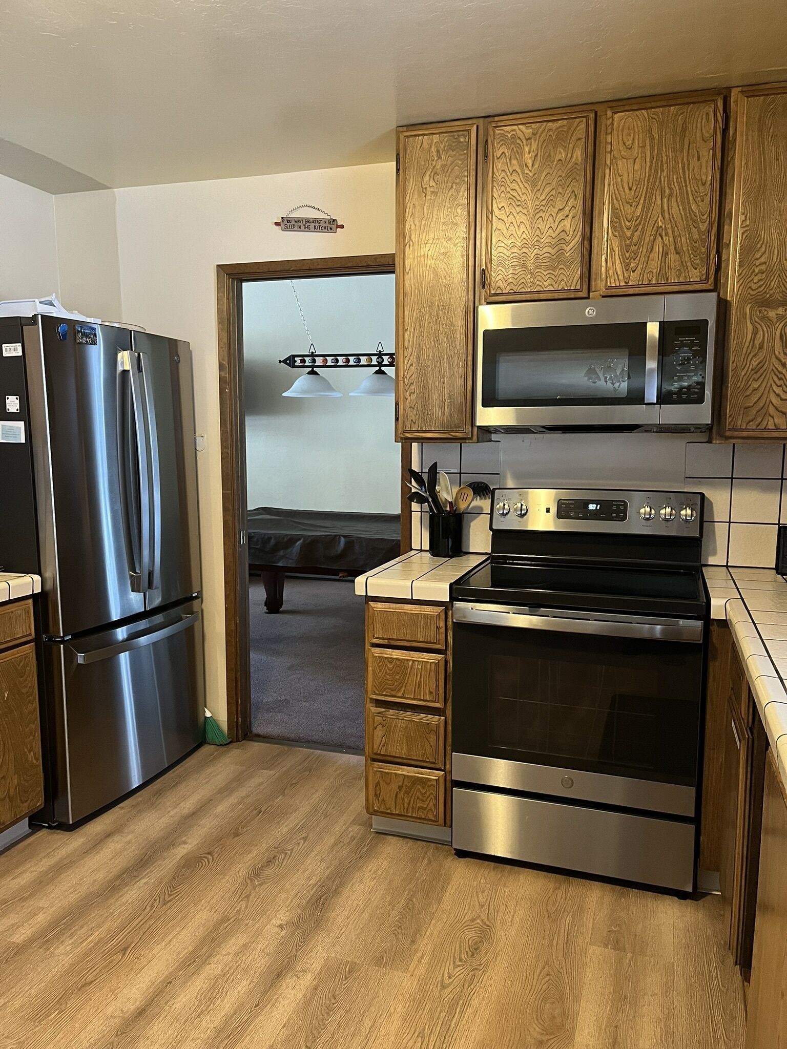 Una cocina moderna con electrodomésticos de acero inoxidable, armarios de madera y una cama visible en la habitación contigua.