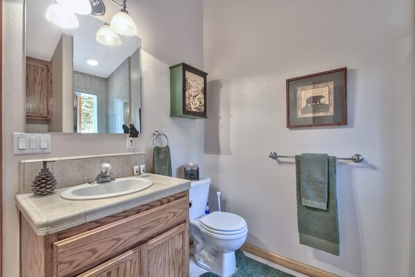 A bathroom with a wooden vanity, a white sink, a toilet, and framed pictures on the wall.