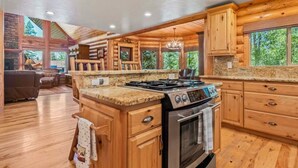A spacious kitchen with wooden cabinets, granite countertops, and a large island with a stove. - Nature's Delight, Private Family-Friendly Cabin (McCall)