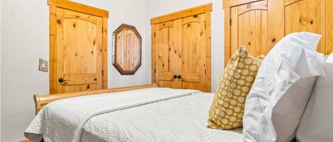 Un dormitori amb llit, roba de llit blanca, panell de fusta i dues portes de fusta.