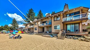 A two-story building with a balcony, a sandy beach in front, and a clear blue sky.