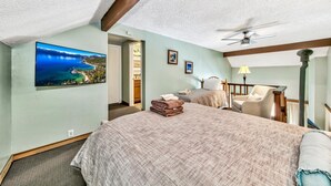 A bedroom with a large bed, a ceiling fan, a view of a lake, and a door leading to a bathroom.
