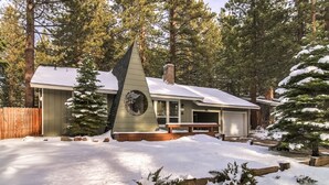 Una cabaña con techo inclinado, rodeada de nieve y altos pinos.