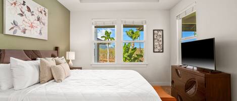 Un dormitorio con cama, ventilador de techo, televisión, cómoda y ventana con vistas a palmeras.