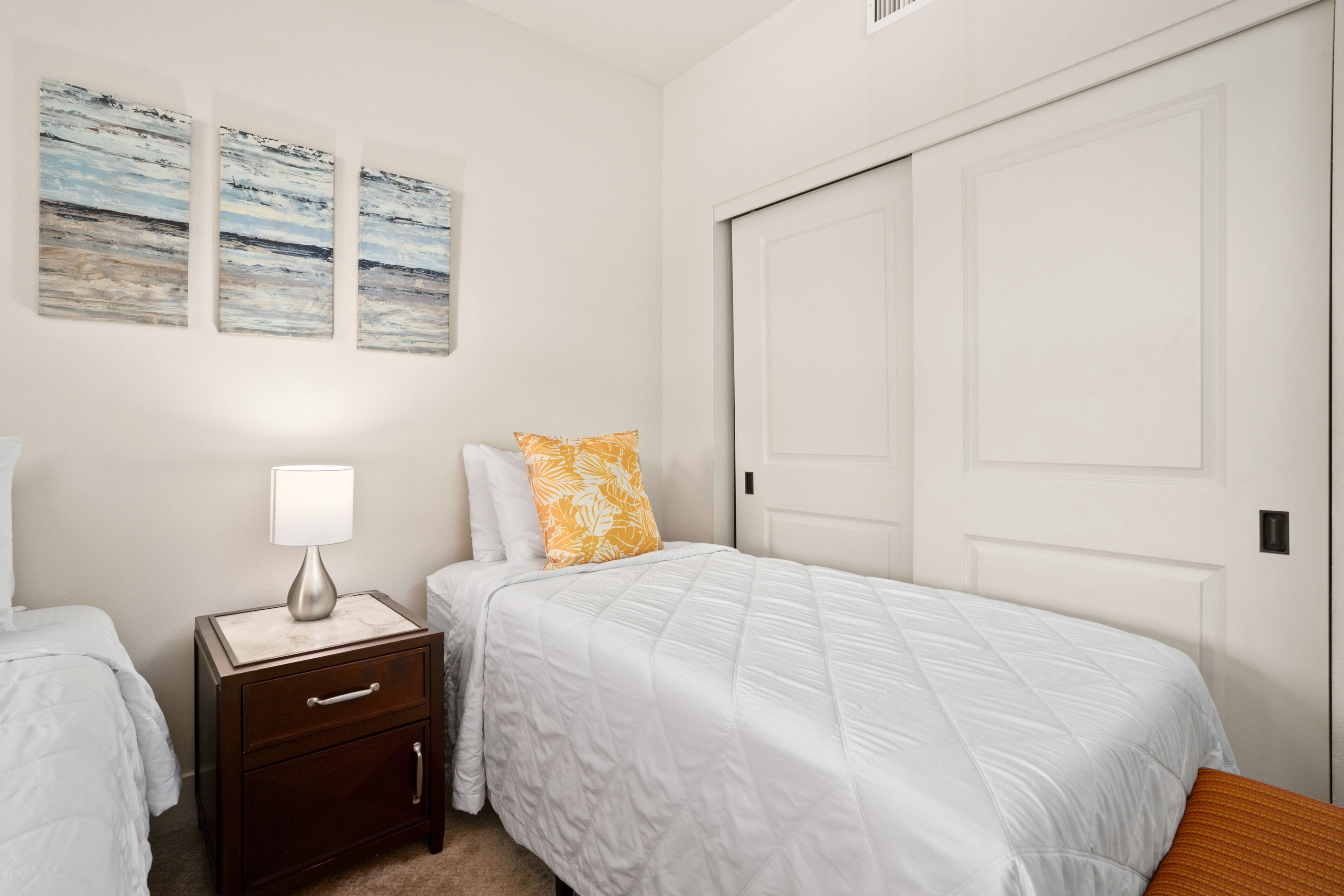 A bedroom with a bed, nightstand, lamp, and artwork on the wall.
