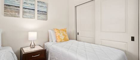A bedroom with a bed, nightstand, lamp, and artwork on the wall.