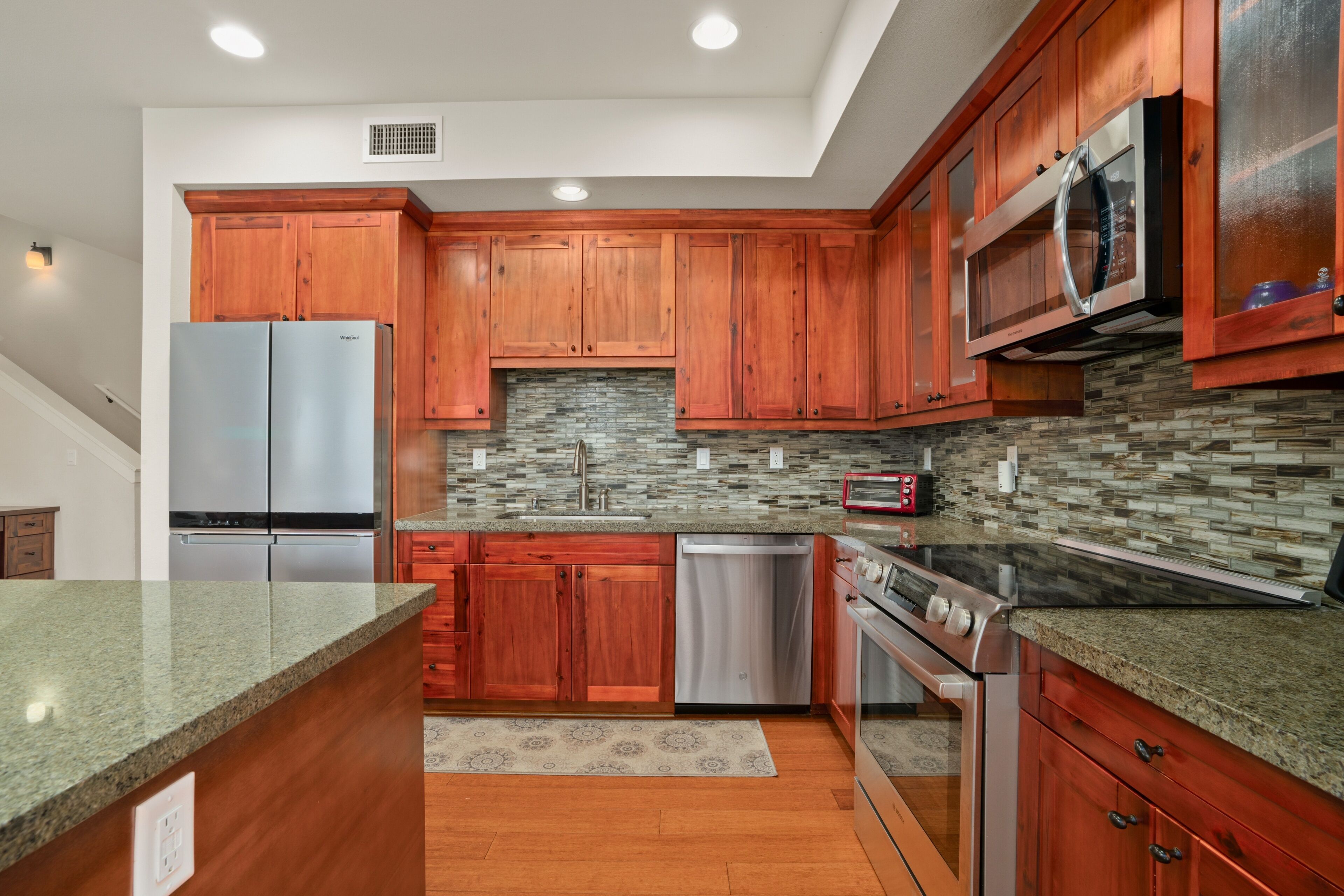 A modern kitchen with wooden cabinets, stainless steel appliances, and a herringbone tile backsplash.