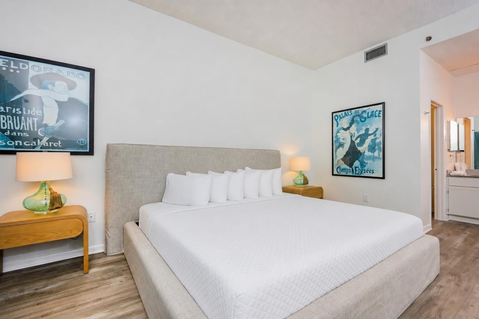 A hotel room with a large bed, two bedside tables with lamps, and two wall-mounted artworks.