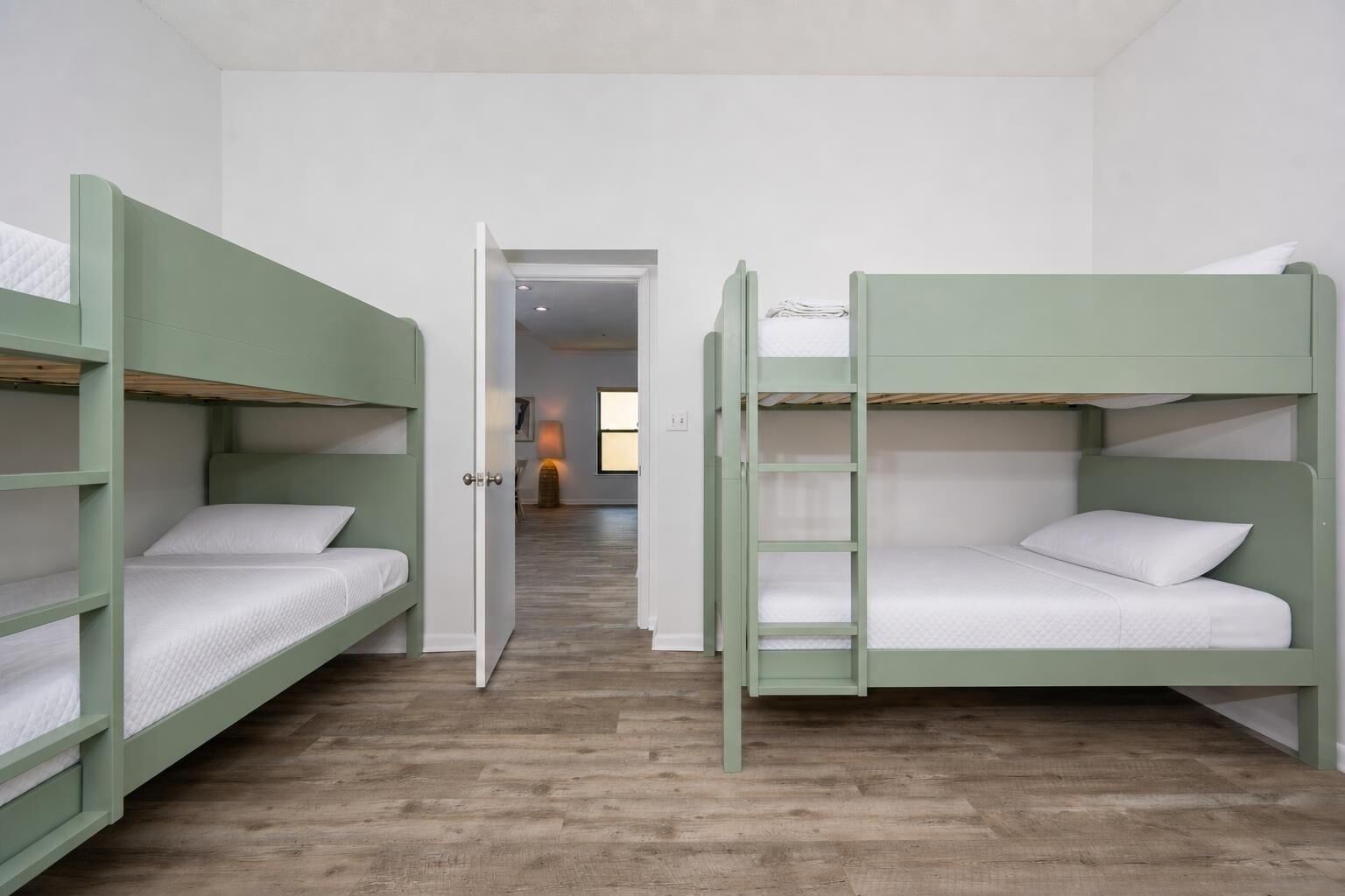A room with bunk beds, a wooden floor, and a door leading to another room.