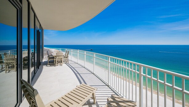 A balcony with a view of the ocean, white railings, and outdoor seating.