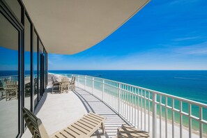 A balcony with a view of the ocean, white railings, and outdoor seating.
