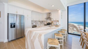 A modern kitchen with a large island, stainless steel appliances, and a view of the beach.
