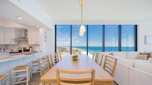 A modern kitchen with a large dining table, white cabinetry, and a view of the ocean.