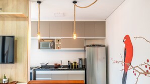 A modern kitchen with a flat-screen TV, stainless steel refrigerator, and a wooden dining table. - Apto Recanto das Aves a 450m da Praia PHA0023 (Ubatuba)