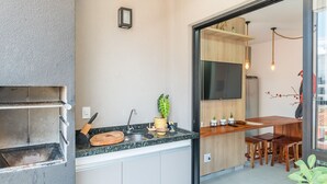 A modern kitchen with a built-in oven, a wooden countertop, and a dining area with a wooden table and chairs. - Apto Recanto das Aves a 450m da Praia PHA0023 (Ubatuba)