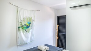 A room with a bed, a towel, a window with blinds, and an air conditioning unit. - Apto Recanto das Aves a 450m da Praia PHA0023 (Ubatuba)