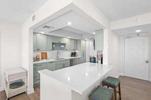 A modern kitchen with a large island, light green cabinets, and white countertops. - Rare Desirable Unit | Located in Shipps Landing III (Marco Island)