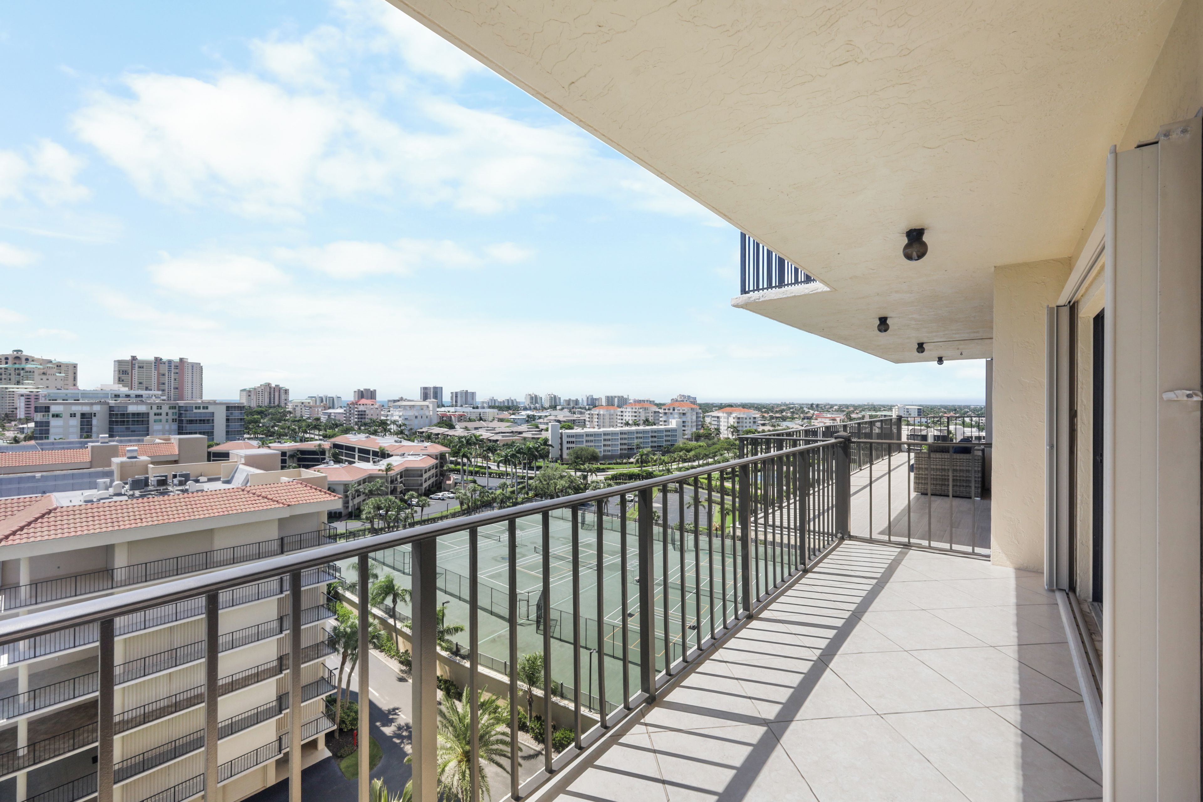 Un balcón con vista a la ciudad, una cancha de tenis y un edificio de varios pisos.