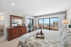 A bedroom with a large bed, a dresser, a chair, and a balcony with a view of the city. - Rare Desirable Unit | Located in Shipps Landing III (Marco Island)