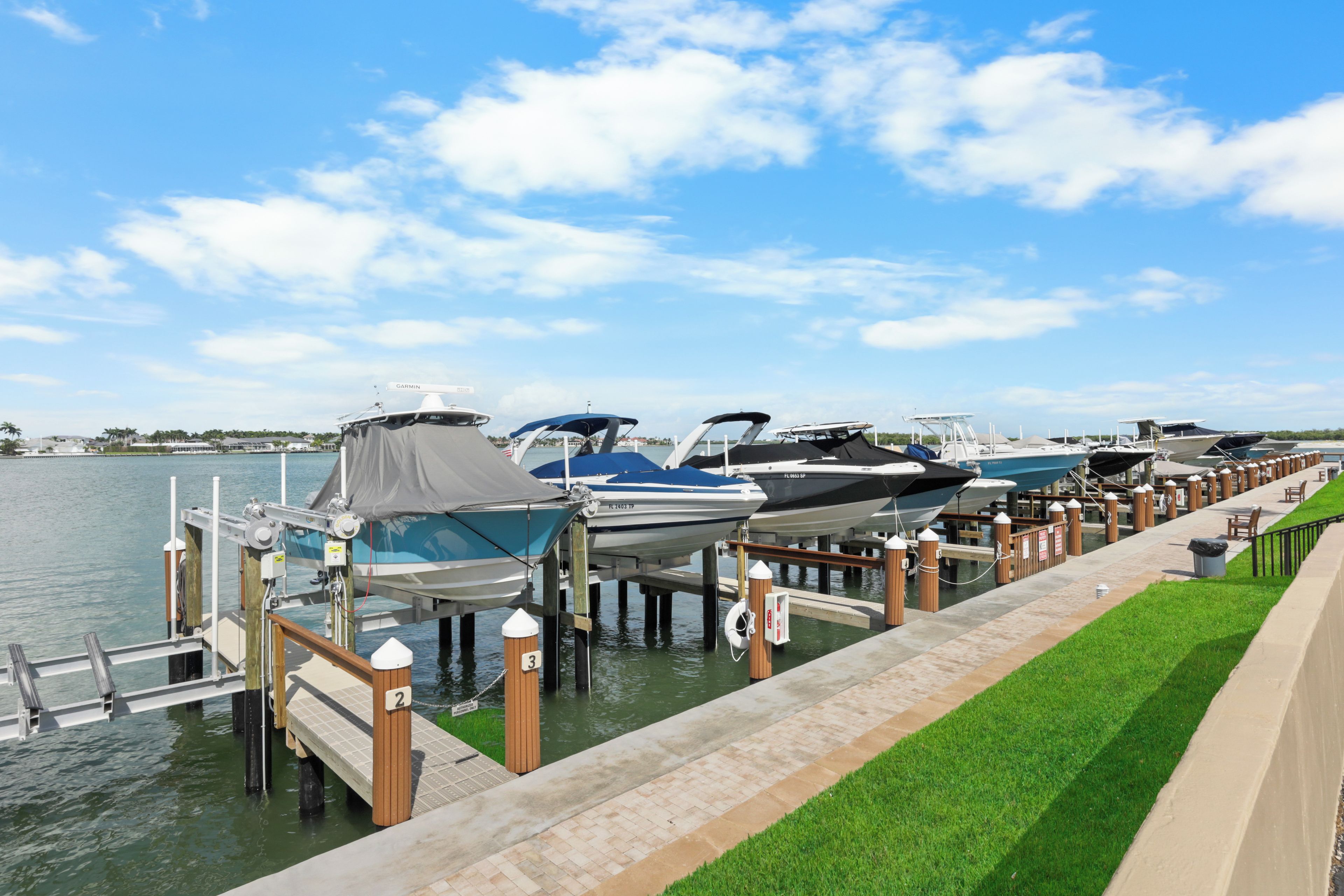 A marina with boats docked at wooden piers, a grassy walkway, and a clear sky.