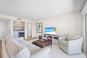 A modern living room with a sofa, ottoman, and a TV on a stand. - Rare Desirable Unit | Located in Shipps Landing III (Marco Island)