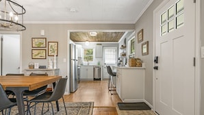 A modern kitchen with white cabinets, stainless steel appliances, and a wooden dining table with chairs. - Cozy Pet-Friendly Cottage w/Mountain Views, Fire Pit, & Fenced Yard! (Waynesville)