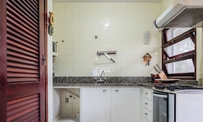 A kitchen with white cabinets, a granite countertop, a stove, and a window with blinds.