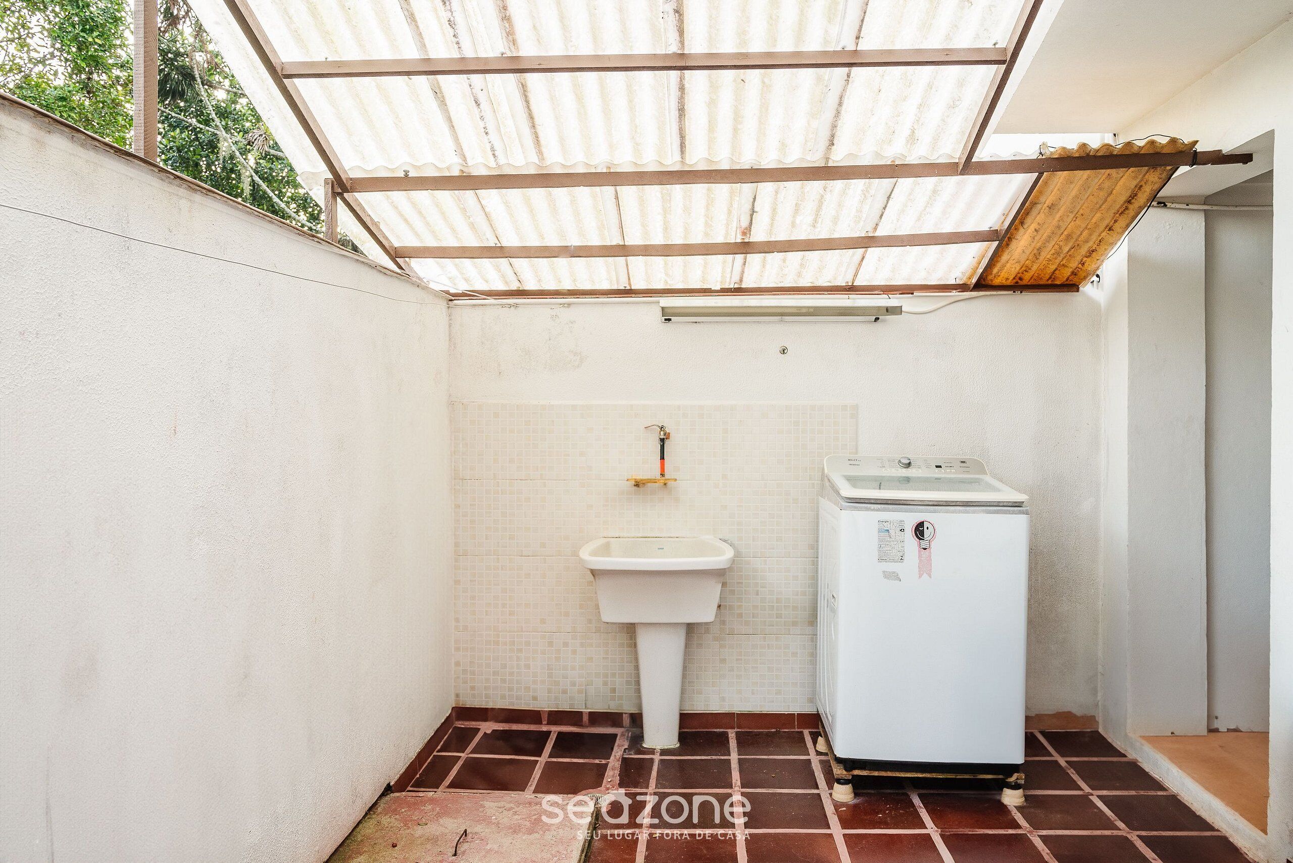 Un baño pequeño con un lavamanos, una lavadora y piso de baldosas.