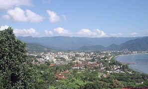 A coastal cityscape with buildings, a body of water, and mountains in the background.
