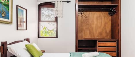 Un dormitorio con cama, ventana con vistas, armario y un cuadro en la pared.