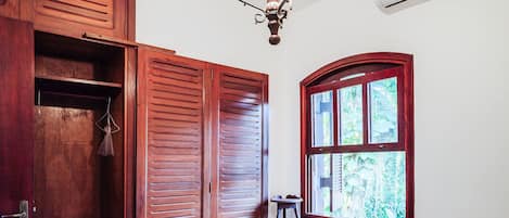 A room with wooden doors, a window with a view of greenery, and a ceiling light fixture.