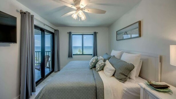 Une chambre à coucher comprenant un lit, une table de chevet, un ventilateur de plafond, une fenêtre et une vue sur l’extérieur.