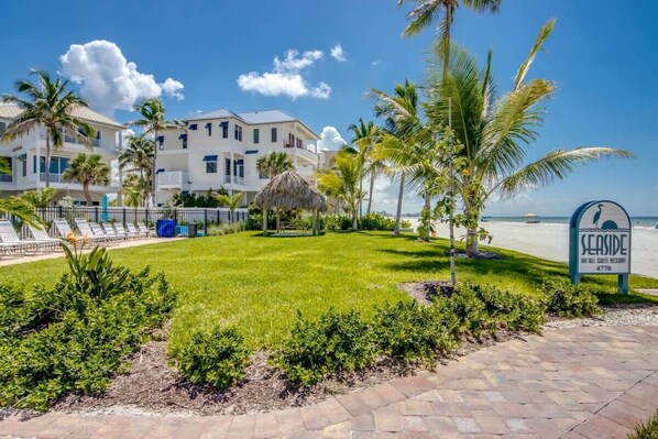 A beachfront hotel with a well-maintained lawn, palm trees, and a sign indicating the name 'SEASIDE.'