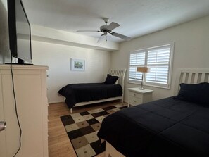 A bedroom with a bed, a nightstand, a ceiling fan, a window with blinds, and a wall-mounted TV. - Waterfront 2B/2B  Condo Royal Pelican. 2 heated Pools Pickleball. Walk to Beach (Fort Myers Beach)