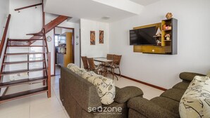 Een woonkamer met een bank, een aan de muur bevestigde televisie en een eethoek met stoelen en een tafel.