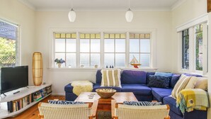 Una sala de estar con un sofá azul, un televisor, una estantería y grandes ventanas con vista al mar.